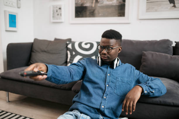 jeune homme afro-américain regardant la télévision à la maison - television boredom men sofa photos et images de collection