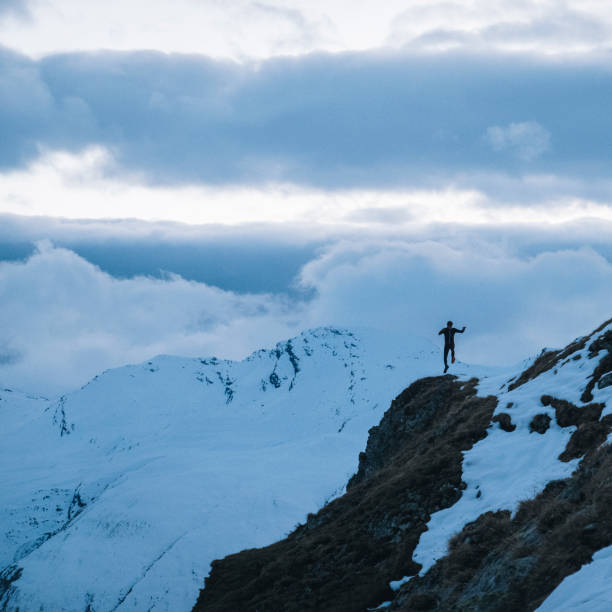 istock Young man trail runs down snowy mountain slope in the morning 1290576656