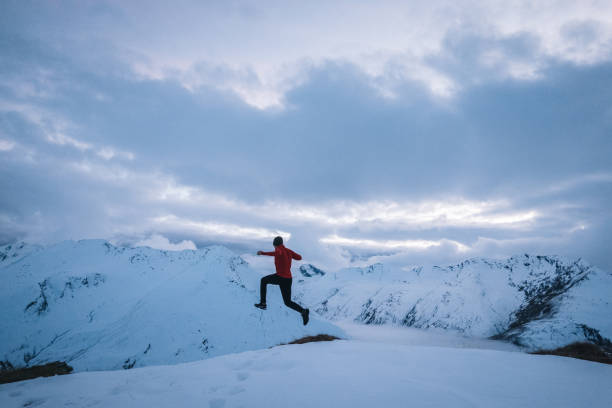 Young man trail jumps down snowy mountain slope in the morning Snowy Swiss Alps in the distance leap of faith stock pictures, royalty-free photos & images