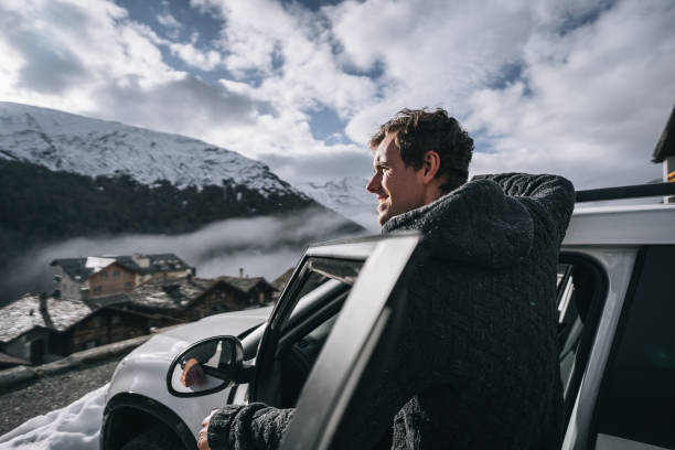 joven se relaja fuera del coche en la carretera nevada de la montaña por la mañana - leaning forward fotografías e imágenes de stock