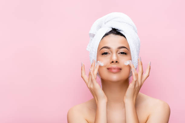 beautiful woman with towel on hair and cosmetic cream on face isolated on pink beautiful woman with towel on hair and cosmetic cream on face isolated on pink face cream stock pictures, royalty-free photos & images