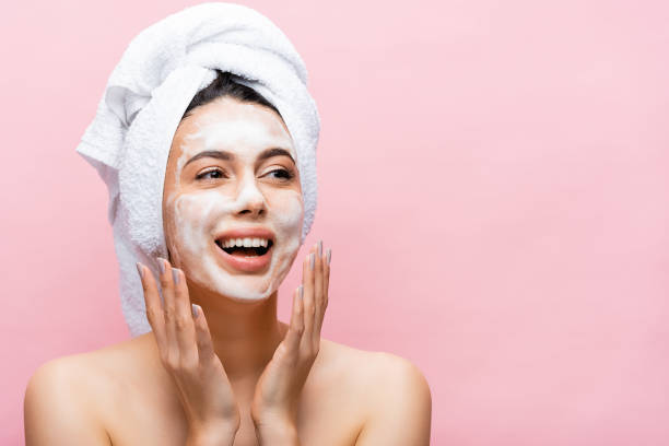 happy beautiful woman with towel on hair and foam on face isolated on pink happy beautiful woman with towel on hair and foam on face isolated on pink washing face stock pictures, royalty-free photos & images