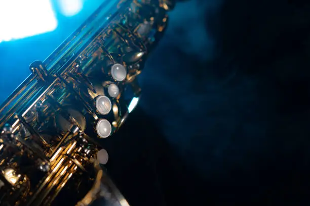 Photo of Golden shiny alto saxophone on black background with blue smoke