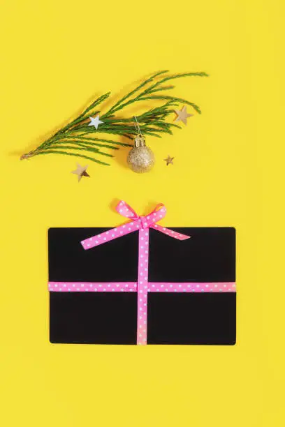 Flat lay gift box shape with a bow made of shop giftcards and golden balls christmas tree branch on trending yellow color background. Creative ideas for presents. Trendy 2021 color vertical background