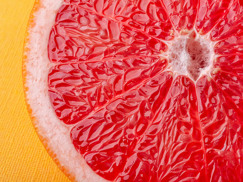 Slice of ripe juicy grapefruit on a yellow background macro shot. Ingredient for fruit desserts. Tasty vegetarian food, slimming diet and vitamin healthy eating. Close-up. Front view.