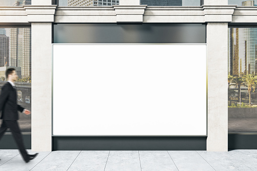 Businessman walking near shop with blank banner on wall. Advertisement and retail concept. Mock up.