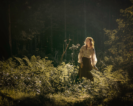 Woman in the woods surrounded by plants and illuminated by natural sunlight