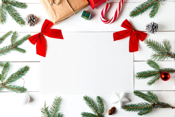 istock Beautiful Christmas composition on wooden white background. Empty card with Christmas present boxes, snowy fir branches, conifer cones, caramel stick, gift. New Year. Top view, copy space. 1290584275
