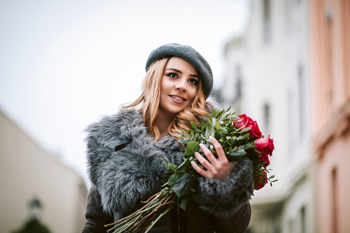 Young beautiful lady enjoys aroma of colorful bouquet of rose flowers. Romantic scents and atmosphere at home, vase stands on desk with laptop. High quality photo