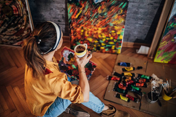 One young beautiful woman, talented artist, painting while drinking coffee at home atelier.