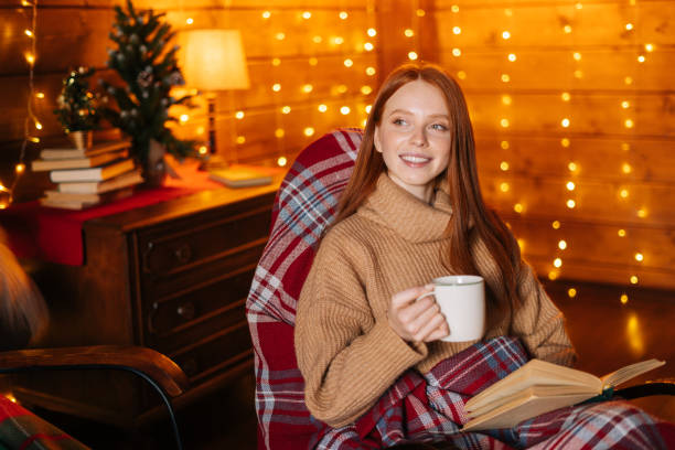 istock Happy young woman drinking hot coffee from cup and reading book while sitting at rocking armchair. 1290588778