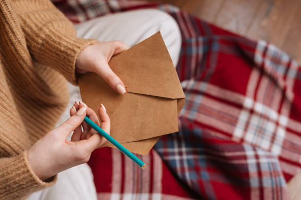 istock Close-up hands of unrecognizable young woman holding empty envelope and pen preparing writing letter 1290588859