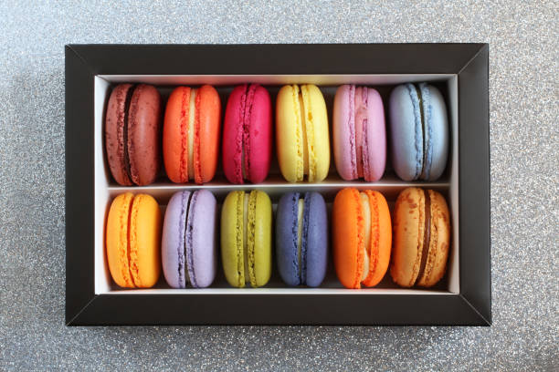 istock Multicolored macarons in a cardboard box without a lid on a silver glitter surface. View from above. Closeup 1290597258