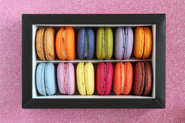 istock Multicolored macarons in a cardboard box without a lid on a pink glitter surface. View from above. Closeup 1290597263
