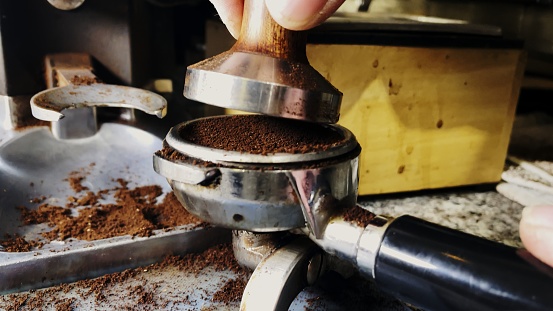 Barista Tamping Ground Coffee to make Espresso in a trendy cafe