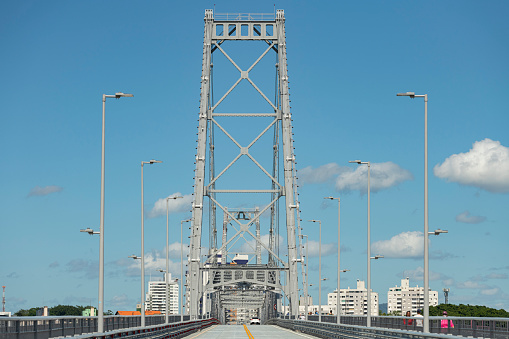 Florianópolis, Santa Catarina, Brazil - November 06, 2020: Front view of the bridge Ponte Hercílio Luz, the longest suspension bridge in Brazil, and one of the 100 largest suspension bridges in the world, along with people a car and buildings in Florianópolis in Santa Catarina state, Brazil