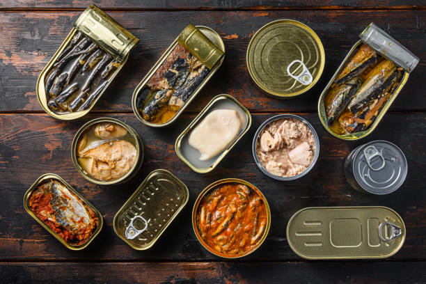 istock Tin cans for fish with different types of seafood, opened and closed cans with Saury, mackerel, sprats, sardines, pilchard, squid, tuna,  over  dark wood old table  flatlay top view 1290602036