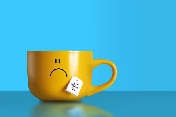 Blue monday tea text with sad smiley face on big yellow cup on blue background. The most depressing day of the year. Blue monday breakfast concept. Copy space.