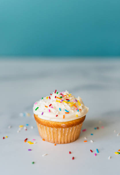 istock Vanilla frosted cupcake with sprinkles with a  blue background. 1290605154
