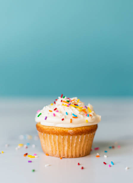istock Vanilla frosted cupcake with sprinkles with a  blue background. 1290605155
