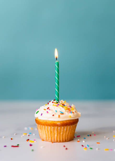 istock Frosted cupcake with sprinkles and candle with a  blue background. 1290605158