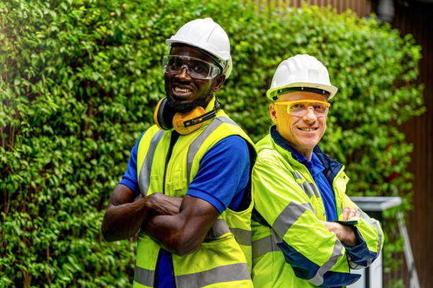 istock team factory worker technician engineer men standing confidence with green working suite dress and safety helmet. Background of green trees wall. 1290606050
