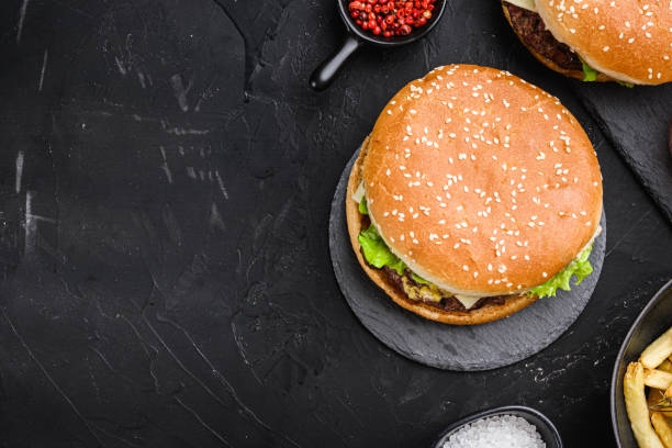 istock Angus burger with cheese, lettuce, and tomato on black background, flat lay with copy space 1290607256