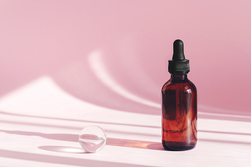 Hyaluronic acid oil mockup. Anti aging serum with collagen and peptides on pink surface with shadows. Sunlight and shadow from cbd oil cosmetic. Transparent liquid product in glass bottle with dropper