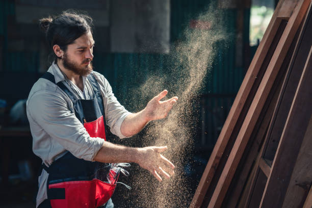 istock caucasian carpenter working in wood workshop clap hands with sawdust diffuse in air. concept of carpenter working in wood workshop 1290616844