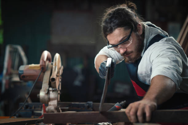 istock caucasian carpenter working in wood workshop cutting wood piece with hand saw on work table in wood workshop. concept of carpenter working in workshop 1290616846