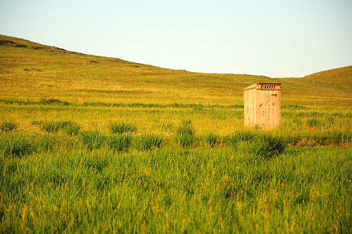 Wooden toilet standing in a field at the foot of a high hill. Close-up.