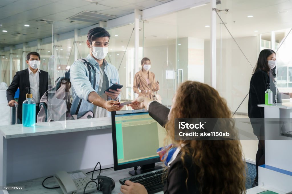 A male airline passengerwith mask is handing over his passport at the airline counter check in through an acrylic barrier for disease prevention coronavirus or covid-19 at airport for New normal travel Airport Stock Photo