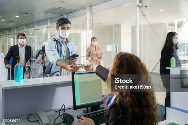 A Male Airline Passengerwith Mask Is Handing Over His Passport At The Airline Counter Check In Through An Acrylic Barrier For Disease Prevention Coronavirus Or Covid19 At Airport For New Normal Travel Stock Photo - Download Image Now