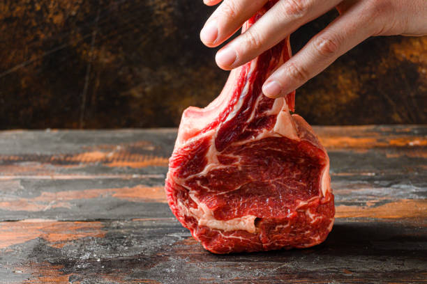 istock Raw tomahawk steak in butcher hands side view over rustic old cutting board with dark planks 1290620458