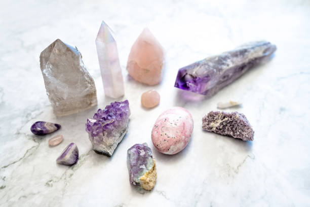 Natural Amethyst and Quartz Crystals on a White Marble Background This is a photo of a variety of pink and purple crystals including amethyst, angel aura quartz, rose quartz, smokey quartz, fluorite, lepidolite, and a rhodonite palm stone on a white marble background. crystal stock pictures, royalty-free photos & images