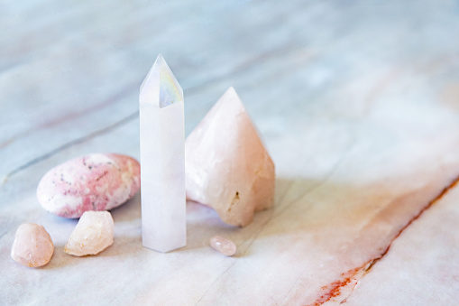 This is a photo of a variety of crystals including an angel aura quartz tower, rose quartz, and a rhodonite palm stone.