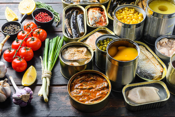 istock Different canned conserve products in tin cans. with fresh organic ingridients Saury, mackerel, sprats, sardines, pilchard, squid, tuna pinapple, corn, peas, mango ,  beans,   over  old wood dark textured background  side view 1290624702