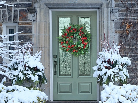 Front door with Christmas wreath with red holly berries on old stone faced house