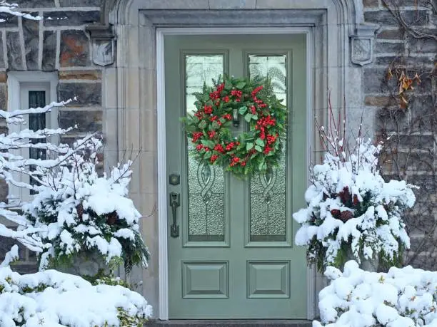 Photo of Front door with Christmas wreath with red holly berries on old stone faced house
