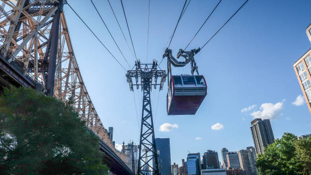 View of flying Roosevelt Island Tramway over city and East River at Manhattan New York Quite amazing to see a flying cable car across the dense city fabric. roosevelt island stock pictures, royalty-free photos & images