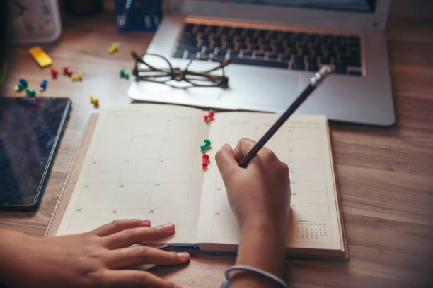 arbeiten von zu hause aus konzept. planer mit tablet und schreiben, um die tägliche agenda im kalenderbuch zu planen. hand der frau markieren und notierte zeitplan (urlaubsreise) auf tagebuch am home-office-schreibtisch. kaffeeplatz auf dem tisch - working at home calendar laptop women stock-fotos und bilder