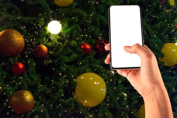 istock Close up hand holding phone isolated on white background with Illuminated  decoration of  Christmas tree with  hanging yellow and red ball. 1290635306
