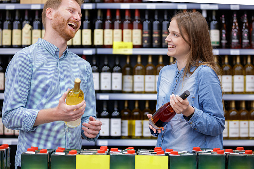 Young couple laughing and trying to agree on the choice of wine, white or rose