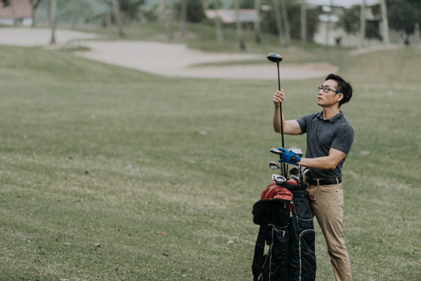 reifen asiatischen chinesischen mann golfer auspacken golfausrüstung im regen auf golfplatz - golf golf course putting green hole stock-fotos und bilder