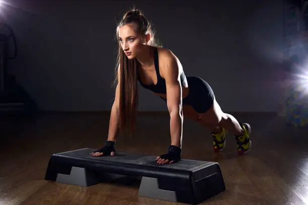 Athletic Beautiful Woman Does Push-up. Cross Fitness and Bodybuilding Gym Training with Aerobic Step.