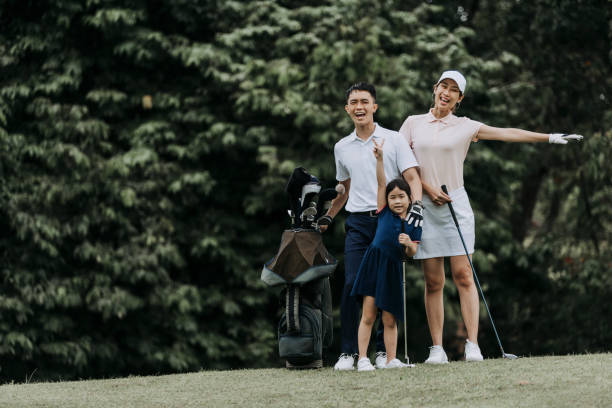 szczęśliwy azjatycki chińczyk para golfista z córką uśmiechając się i patrząc na kamerę na polu golfowym - standing family golf loving zdjęcia i obrazy z banku zdjęć