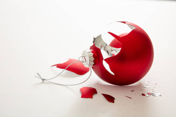 A close-up view of a shiny red glass Christmas ornament with a golden hook. The ornament has a glossy, reflective surface with subtle swirls, creating a festive holiday aesthetic.