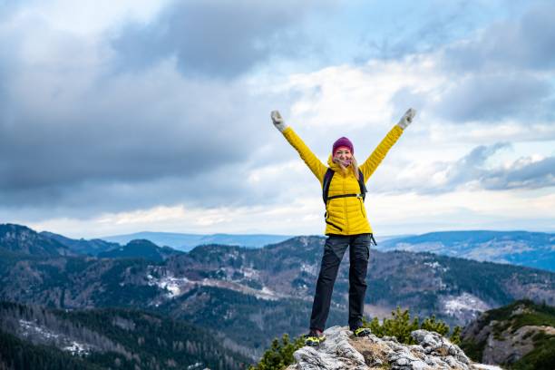 Successful hiker woman in a yellow down jacket on the top.