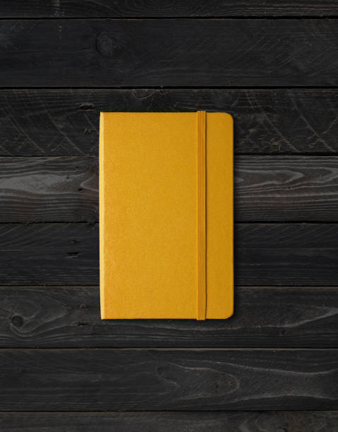 istock Yellow closed notebook on black wood background 1290655415