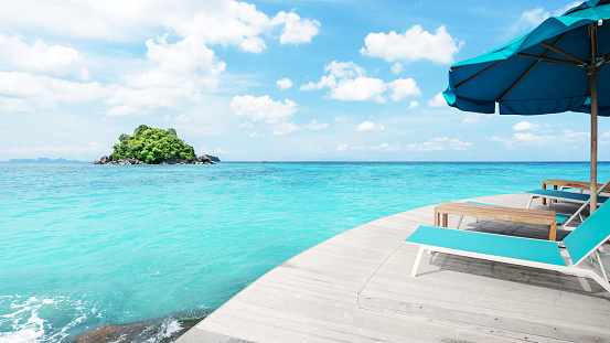 Lounge chairs and umbrella on the wooden balcony terrace beside turquoise sea